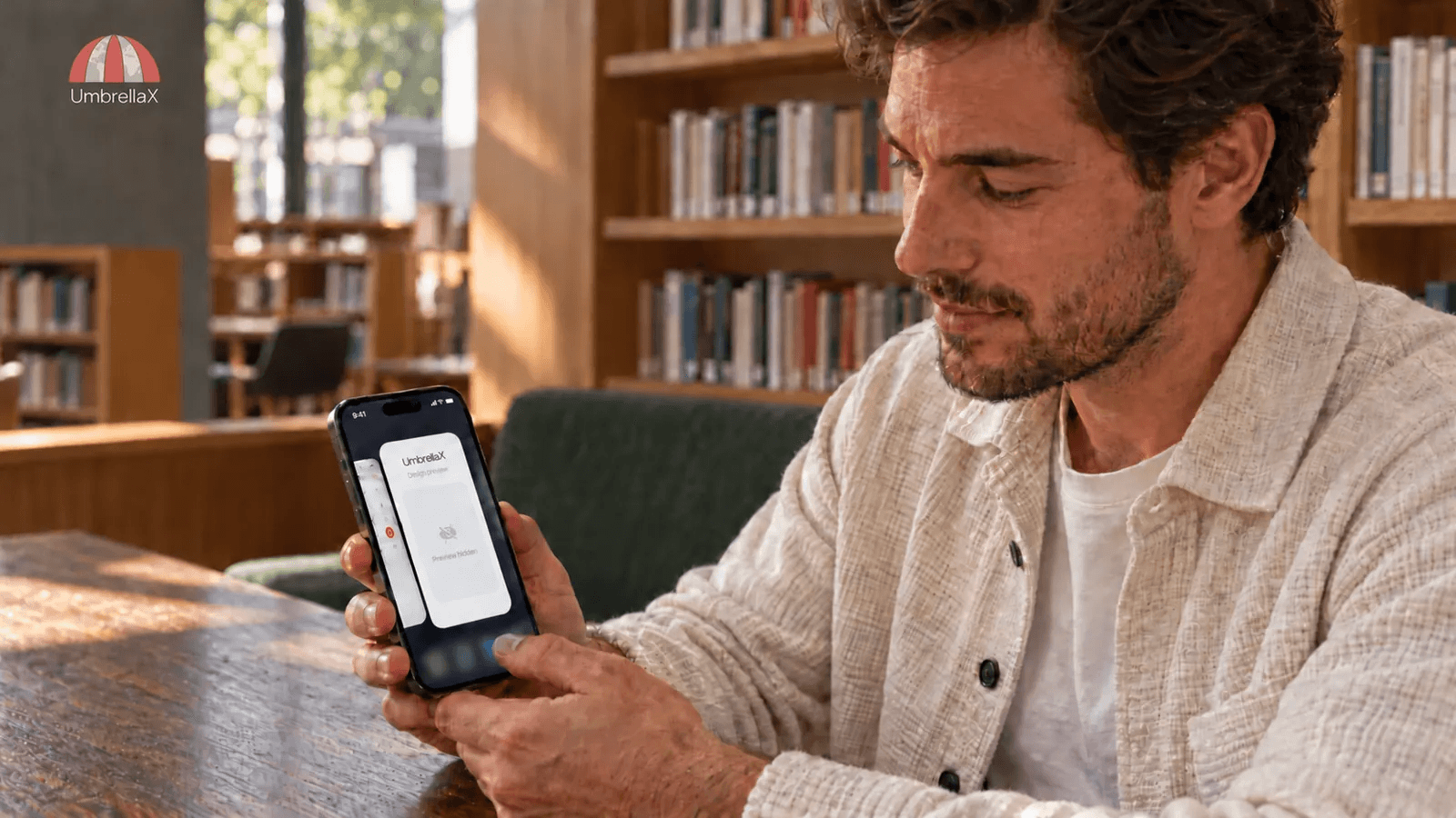 A reader checks a concealed UmbrellaX app-switcher preview on an iPhone in a sunlit library.